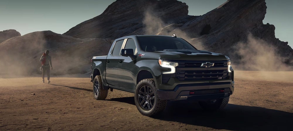 A person with climbing gear walking toward a black 2026 Chevrolet Silverado 1500 truck in the desert