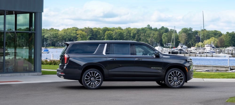 A side view of a gray 2027 Chevrolet Suburban SUV parked at a marina