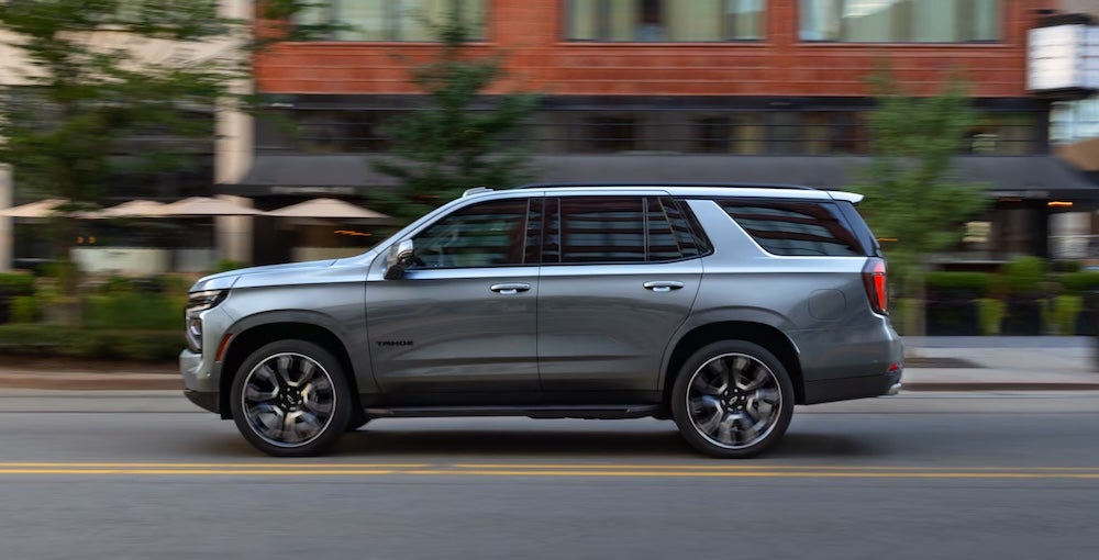A side view of a gray 2027 Chevrolet Tahoe SUV driving down a city street