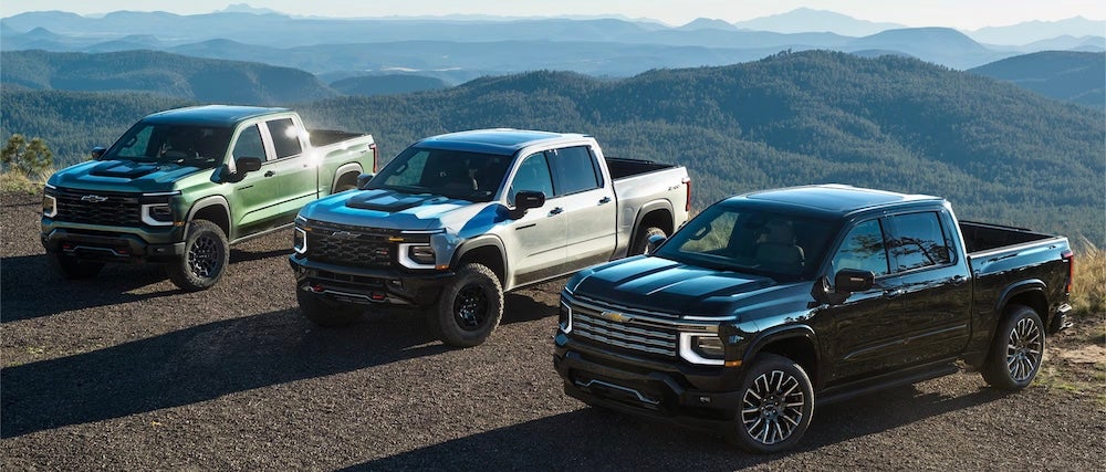 Three 2027 Chevrolet Silverado pickup trucks parked on a mountain ledge